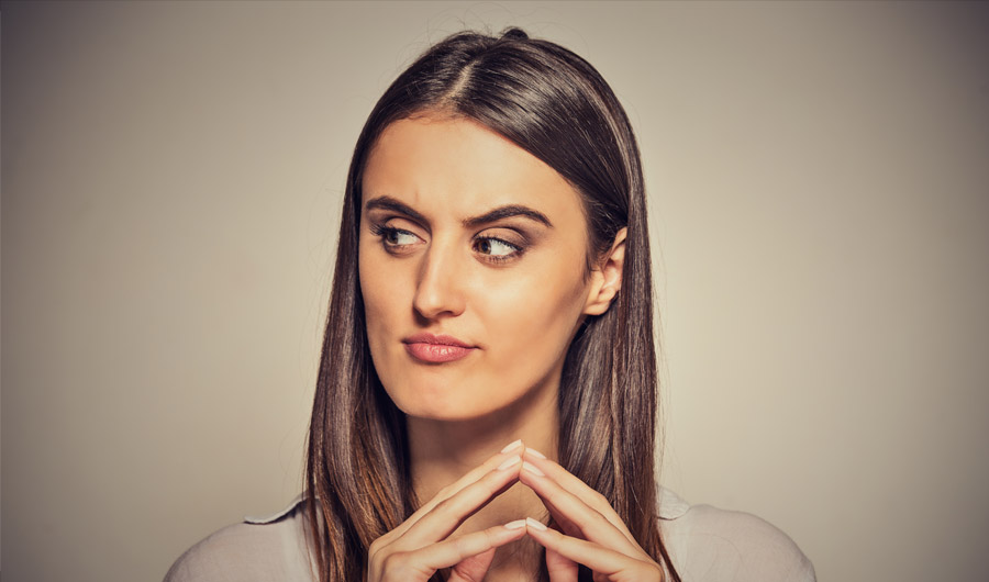 Woman glancing sideways with raised eyebrows and arched fingers, looking sneaky.