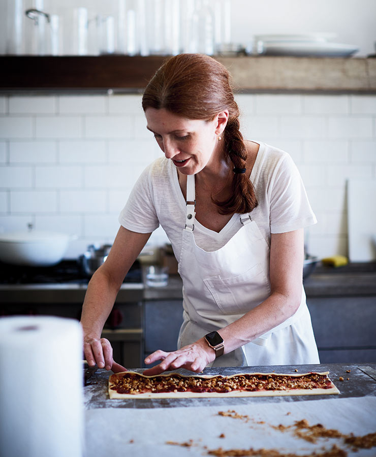 Baker Melissa Weller stands at a counter rolling dough around a filling.