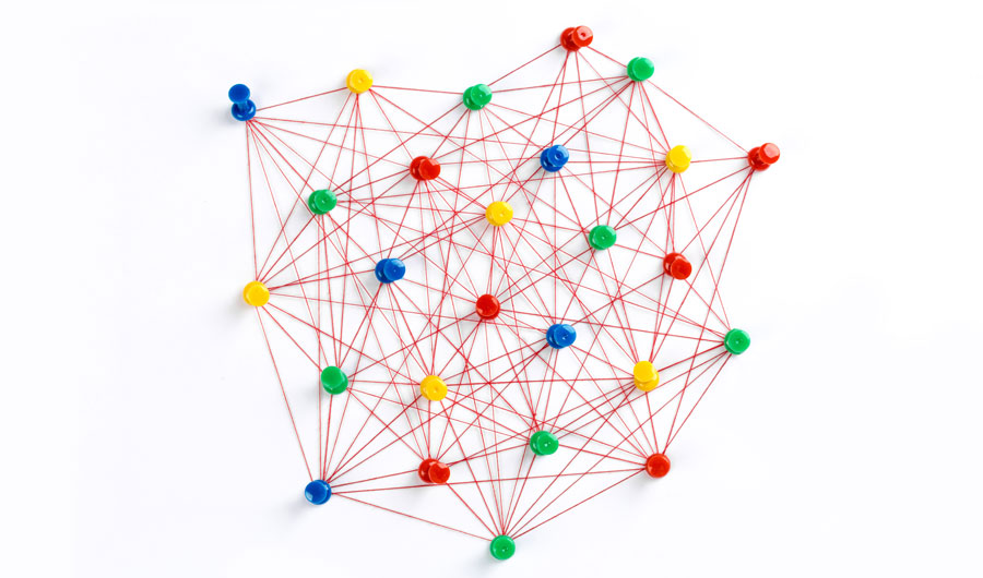 A network made from different colored push pins connected with red thread 