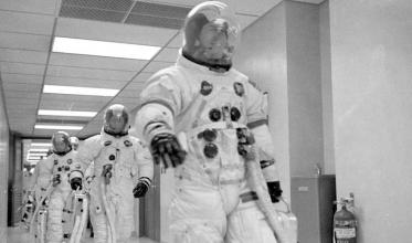 Apollo 13 astronauts Lovell, Swigert, and Haise walk towards the transfer vans in their astronaut suits.