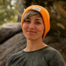 Portrait of writer Jude Coleman, wearing a t-shirt and an orange knit hat.